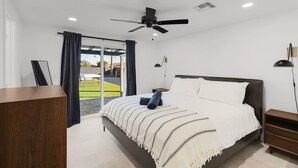 Et moderne hotelværelse med en stor seng, ventilator, skrivebord og udsigt til en tennisbane.