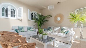 Ein Wohnzimmer mit zwei weißen Sofas, Korbstühlen, einem Marmortisch und Topfpflanzen.