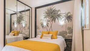Ein Hotelzimmer mit einem Bett, einem Nachttisch, einem Spiegel und einem Wandbild mit Palmen.