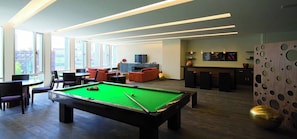A modern indoor pool area with a pool table, seating, and a bar area.