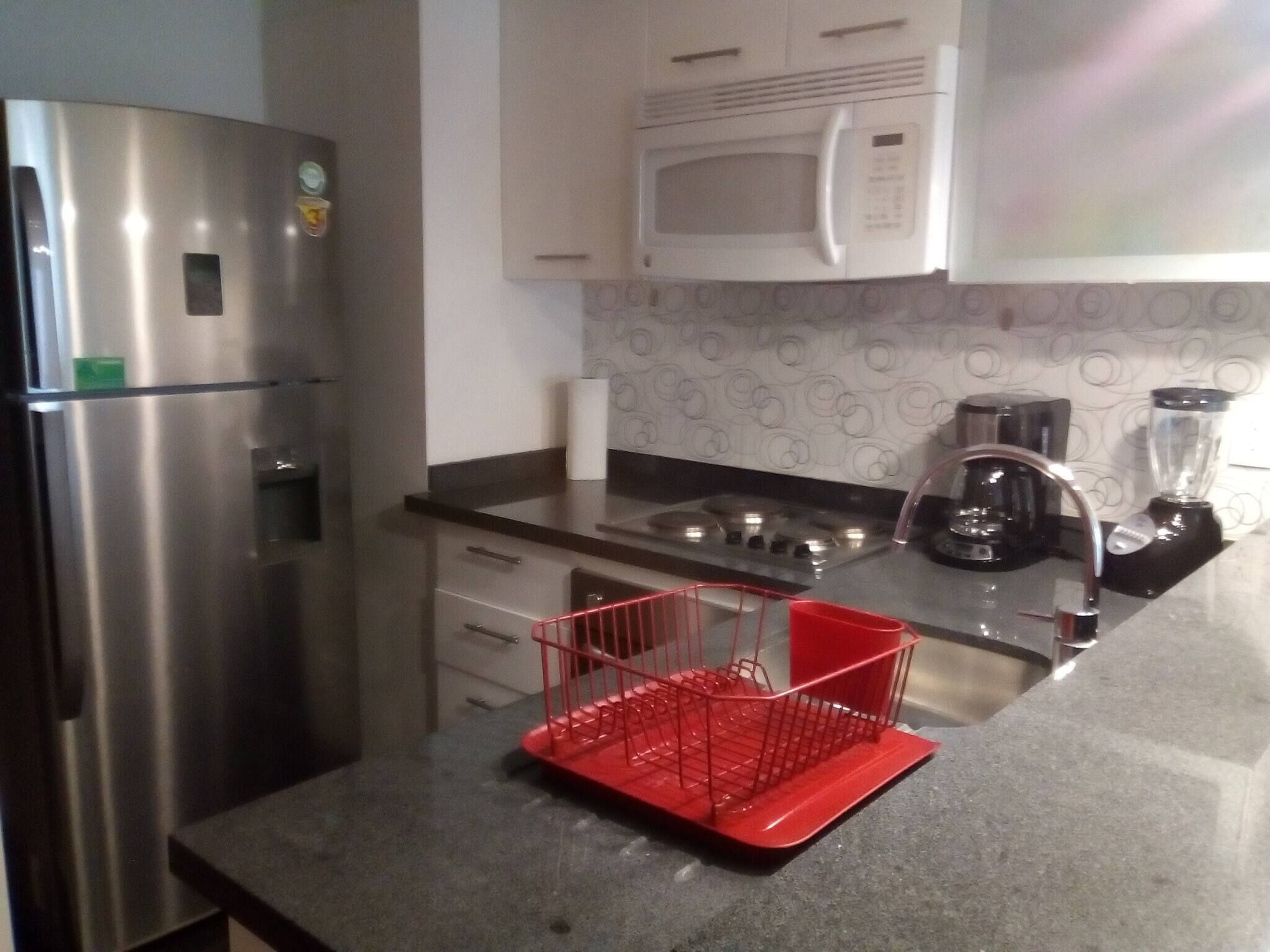 Een keuken met roestvrijstalen apparatuur, een magnetron, een fornuis en een rode keukenorganisator.