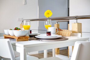 A breakfast table with white chairs, a white table, and a metal railing in the background.