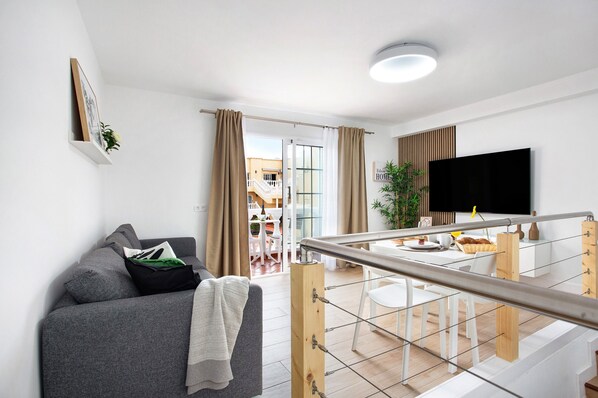 A modern living room with a sofa, a flat-screen TV, and a dining area with a table and chairs.