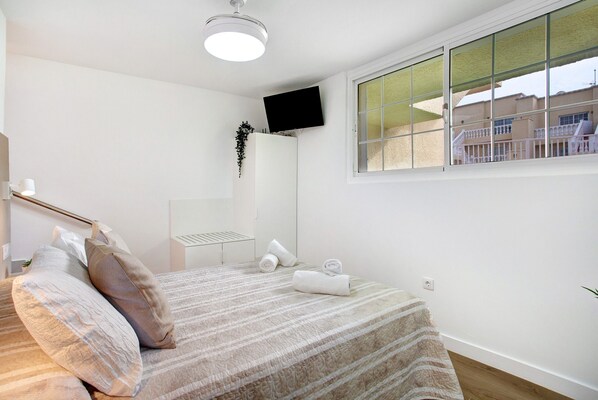 A bedroom with a bed, a TV mounted on the wall, a window with a view, and a plant on the wall.