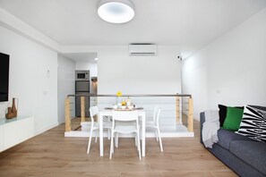 A modern living space with a dining area, a sofa, and a kitchen in the background.