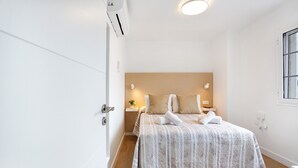 A bedroom with a bed, bedside tables, a nightstand, a wall-mounted air conditioner, and a window. - Holiday Apartment 'Liomor Luxury' with Shared Pool, Wi-Fi and Air Conditioning (Caleta de Fuste)