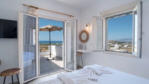 Une chambre d’hôtel avec un lit, une télévision, un balcon équipé d’un parasol et une vue sur la mer.