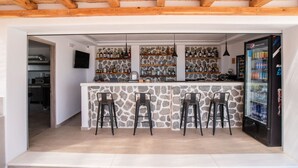 Un coin bar avec des étagères en pierre, trois tabourets, un réfrigérateur et un téléviseur.