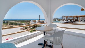 Un balcón con sillas y mesa blancos, con vistas a una piscina y un paisaje pintoresco.