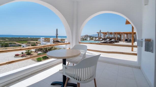 Un balcón con mesa y sillas, con vista a una piscina y zona de descanso con una vista despejada del mar.