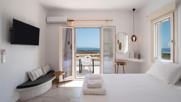 Ein Schlafzimmer mit Bett, einer Bank, einem Fernseher, einem Spiegel und Blick ins Freie.