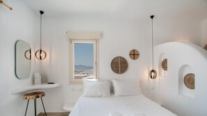 Ein Hotelzimmer mit Bett, einem Holzschemel, einem Fenster mit Blick und Wanddekoration.