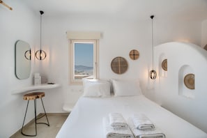 A hotel room with a bed, a wooden stool, a window with a view, and wall-mounted decor.