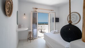 Ett modernt sovrum med en säng, en hängande lampa i form av ett rep, en rund, vävd väggdekoration, ett litet bord med en stol och en skjutdörr i glas som leder ut till en sittplats utomhus.