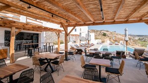 An outdoor seating area with wooden tables and chairs, a pool, and a view of the landscape.