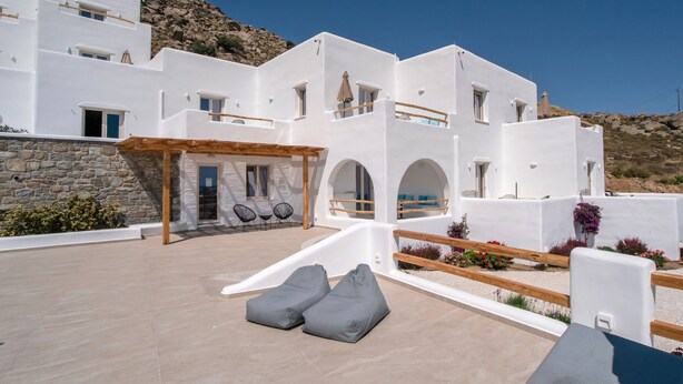 A white building with multiple balconies, a covered outdoor seating area, and a stone wall.