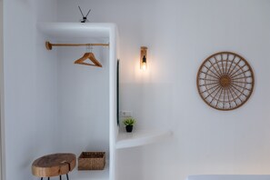 Une salle de bain minimaliste avec un porte-serviettes en bois, un luminaire fixé au mur, un élément décoratif mural, une petite plante en pot et un tabouret en bois.