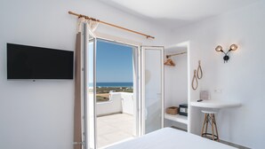 A bedroom with a bed, a TV, a bedside table, a hanging light, a wardrobe, and a view of the sea.