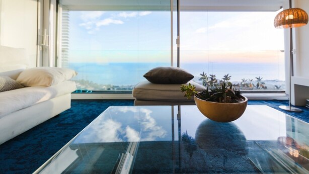 A modern living room with a glass coffee table, a white sofa, a beige cushion, and a view of the ocean. - Apartment 'Sitges Suites B' with Sea View, Wi-Fi and Air Conditioning (Sitges)
