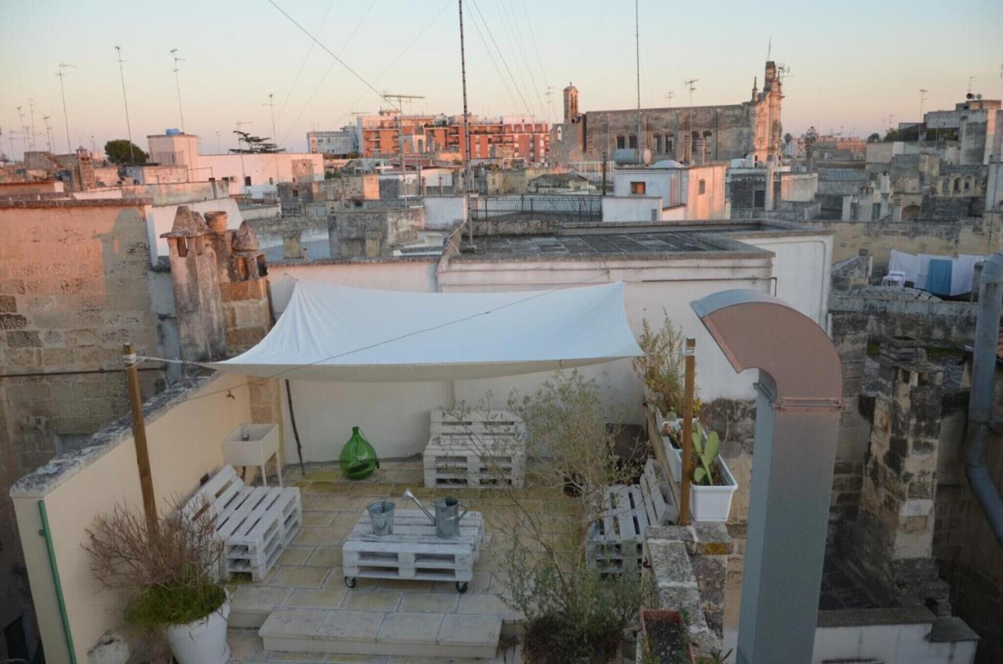 A rooftop terrace with a white canopy, potted plants, and a seating area.