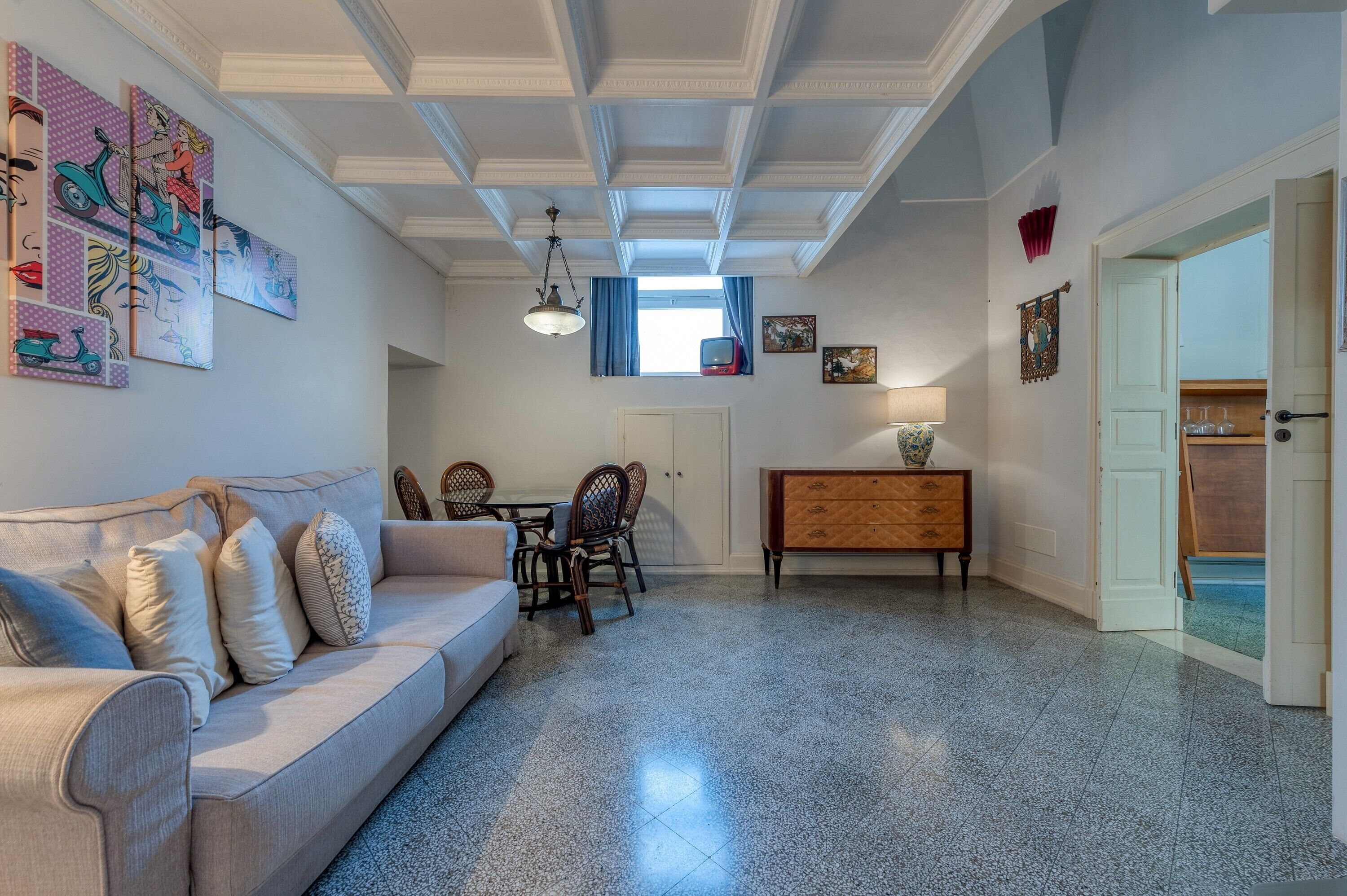 A living room with a sofa, dining table, chairs, a wooden cabinet, and artwork on the walls.