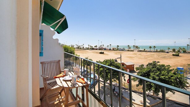 A balcony with a view of a beach, a chair, and a table with items on it. - Apartment 'La Barca' with Shared Terrace, Wi-Fi, and Air Conditioning (Chipiona)