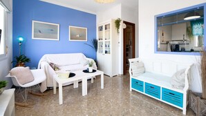 A living room with a blue wall, white furniture, a white sofa, a coffee table, and a wicker ceiling light. - Apartment 'La Barca' with Shared Terrace, Wi-Fi, and Air Conditioning (Chipiona)