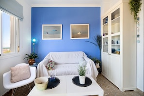 A living room with a blue wall, white furniture, two framed pictures, a white cabinet, and a potted plant. - Apartment 'La Barca' with Shared Terrace, Wi-Fi and Air Conditioning (Chipiona)