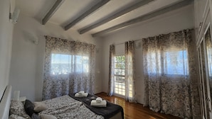 Een kamer met een bed, een tafel met handdoeken, gordijnen met een patroon, en een raam met uitzicht.