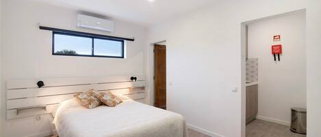 Een slaapkamer met een bed, nachtkastje, raam en een airconditioning.