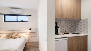 A compact room with a bed, a kitchenette with wooden cabinets, a microwave, and a dishwasher. - Apartment 'Seashel' with Shared Terrace, Wi-Fi and Air Conditioning (Moncarapacho)