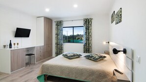 Ein Schlafzimmer mit Bett, Schreibtisch, Fernseher und einem Fenster mit Vorhängen.