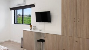 Una habitación con un ventanal grande, un televisor de pantalla plana montado en la pared, un armario de madera y un taburete pequeño.