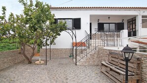 A courtyard with a tree, a wooden bench, a metal staircase, and a building with a tiled roof. - Apartment 'Sunset' with Shared Terrace, Wi-Fi and Air Conditioning (Moncarapacho)