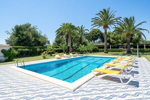 Una piscina con sillas de descanso, palmeras y una terraza con baldosas.