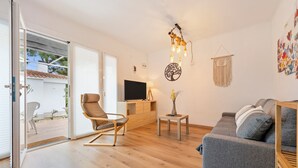 Een moderne woonkamer met een bank, een fauteuil, een televisie, een bijzettafeltje met een vaas en een wandmacramé.