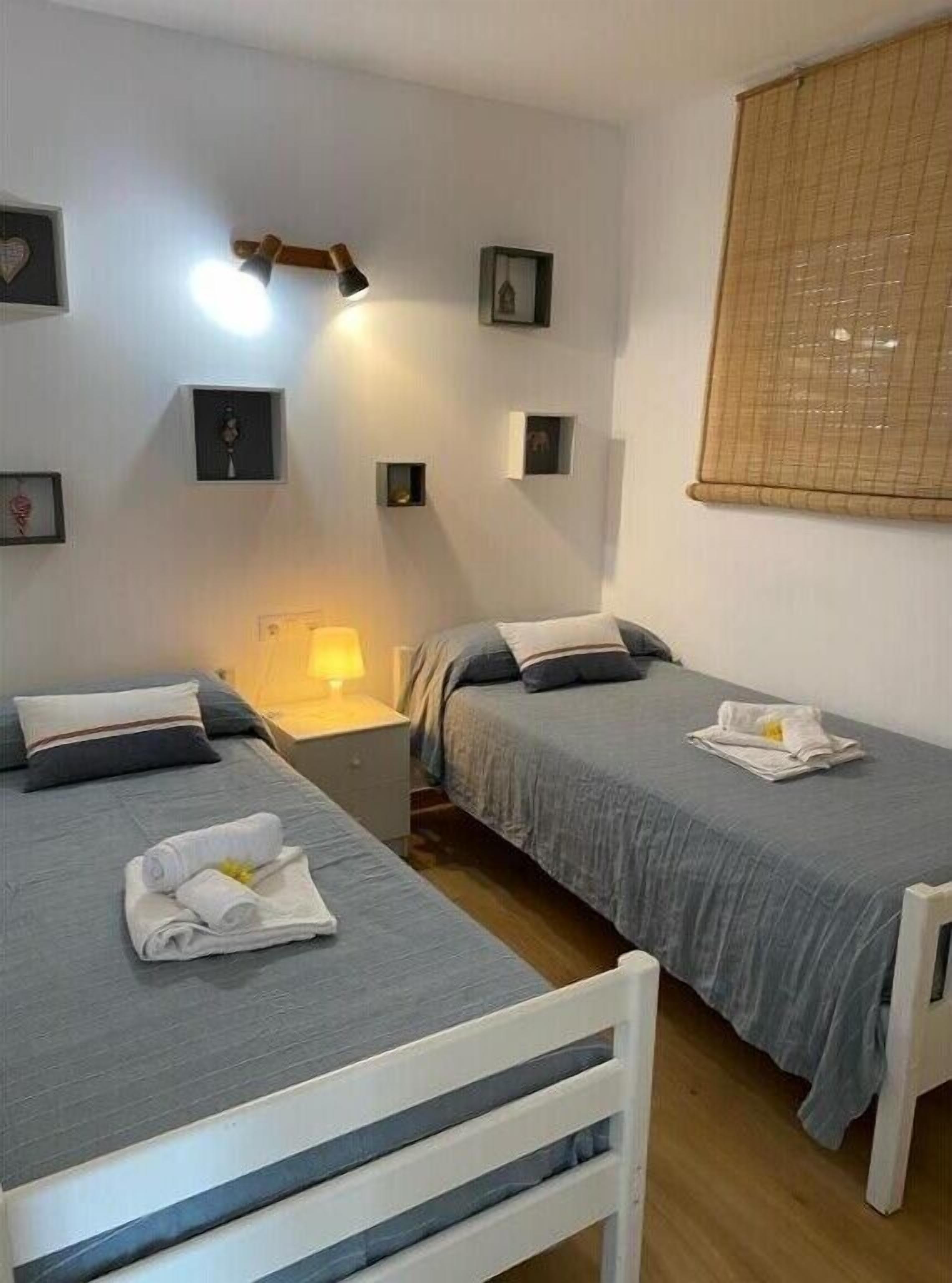 A room with two beds, a nightstand, a lamp, and a window with blinds.
