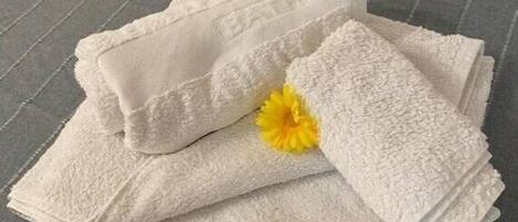 A stack of white towels with a yellow flower on a grey textured surface.