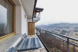 Un balcon avec un banc en bois, une vue sur une vallée et une rambarde en métal.