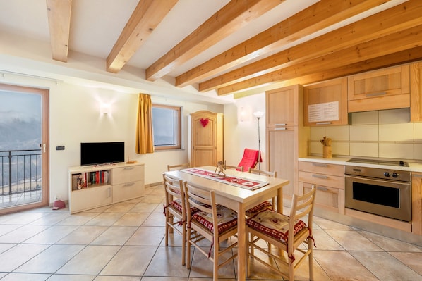 Une cuisine moderne avec des meubles en bois, une table à manger avec des chaises, un téléviseur et un balcon avec vue.