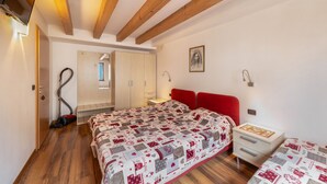 Een slaapkamer met een houten plafond, een bed met een quilt met een patroon, een nachtkastje, een rood hoofdeinde, en een stofzuiger.