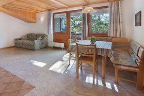 A cozy room with a wooden ceiling, a sofa, a dining table with chairs, and large windows with curtains. - Holiday Apartment 'Appartements Egart 1' with Lake View, Balcony and Wi-Fi (Reschen)
