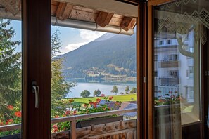 A view from a balcony with a wooden railing, a mountain in the background, and a body of water. - Holiday Apartment 'Appartements Egart 1' with Lake View, Balcony and Wi-Fi (Reschen)