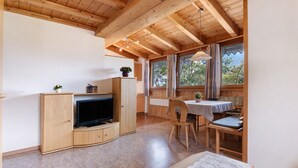 A wooden interior with a television on a stand, a dining table with chairs, and a window with curtains. - Holiday Apartment 'Appartements Egart 2' with Lake View, Balcony and Wi-Fi (Reschen)
