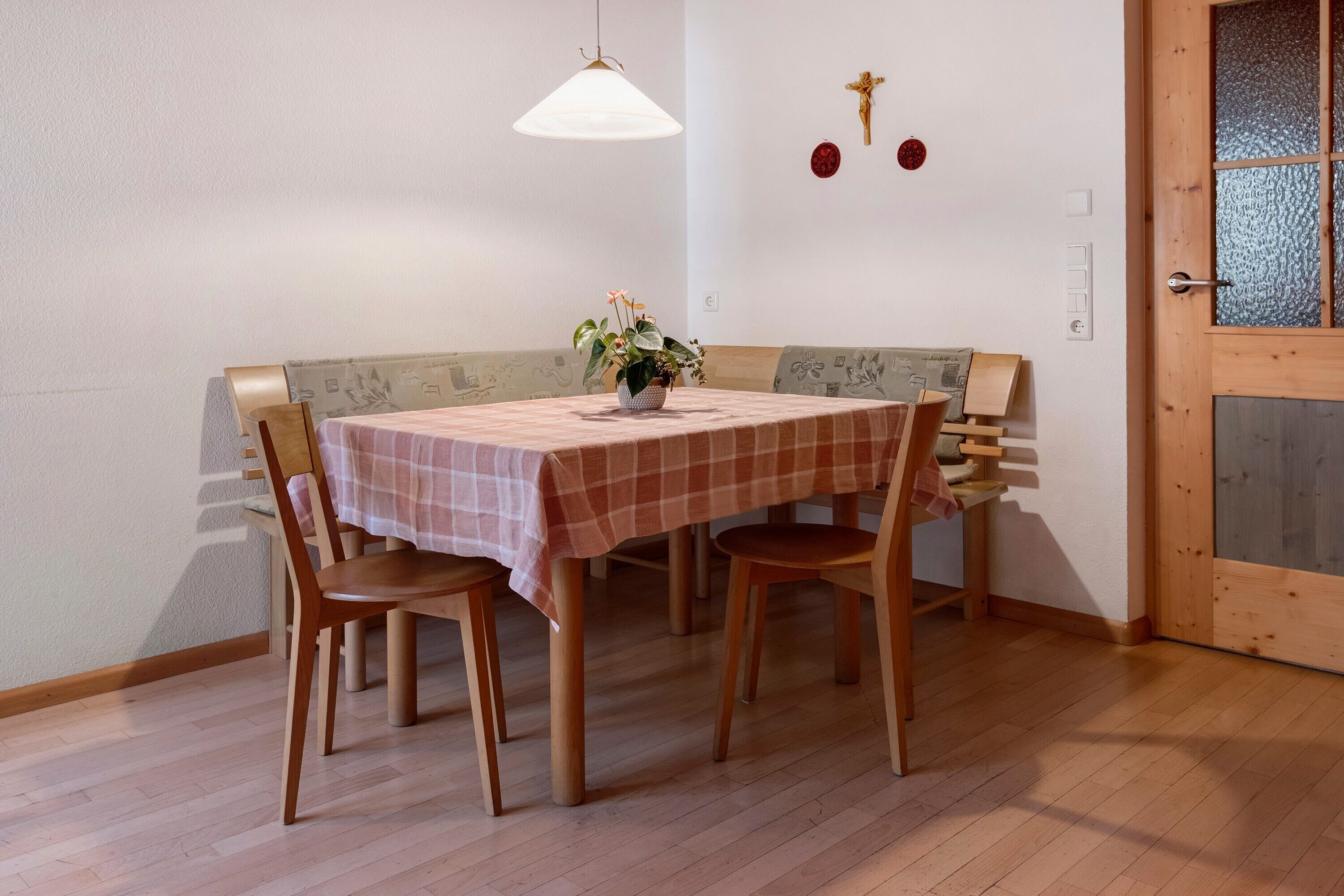 A dining area with a table, chairs, a bench, a hanging light, and wall decorations.