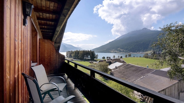 Un balcon en bois, agrémenté de chaises, qui offre une vue sur un paysage montagneux et un lac.