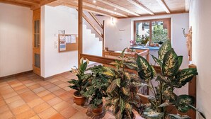 Une pièce spacieuse avec un escalier en bois, des plantes en pot et un tableau d’affichage au mur.