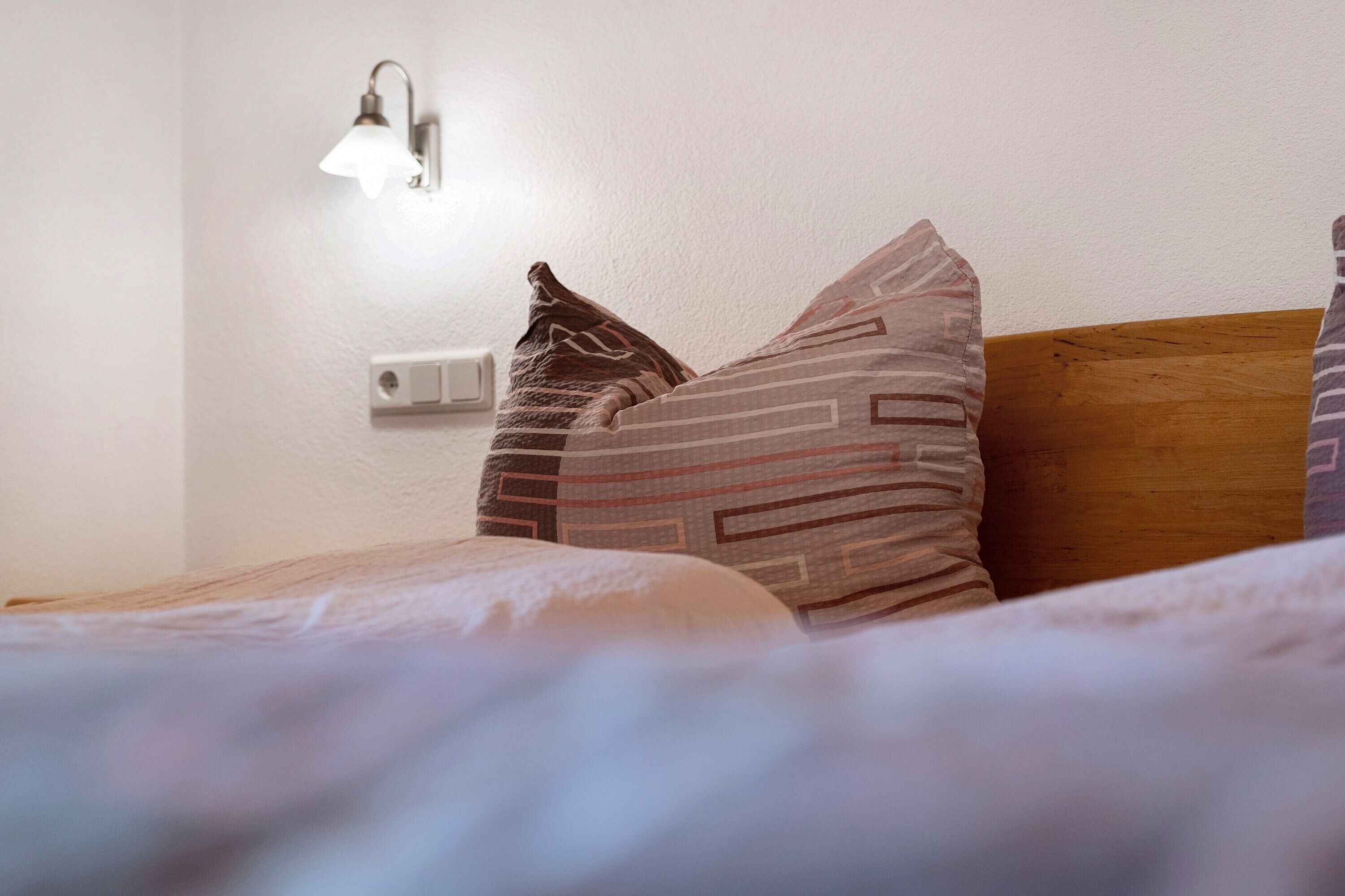 A bedroom with a wooden headboard, a bedside lamp, and patterned pillows.