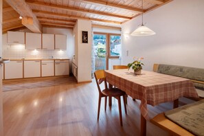 A dining area with a table set for two, wooden flooring, and a view of the outside through a glass door.