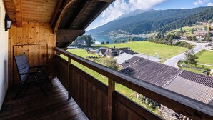 Een houten balkon met uitzicht op een meer, bergen en een dorp.